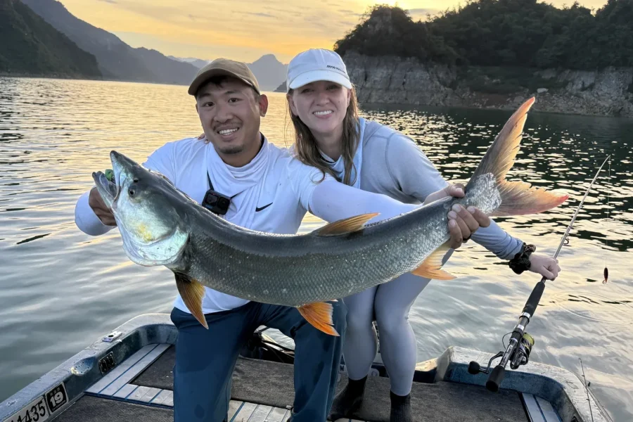 Erin and Brendon holding a trophy yellowcheek on the boat at sunset